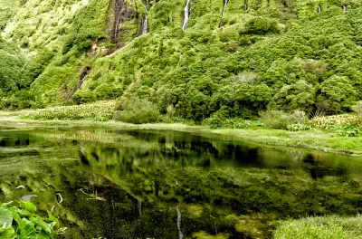 Still lagoon reflecting lush green slopes and waterfalls at Poço da Ribeira do Ferreiro on Flores Island in the Azores.