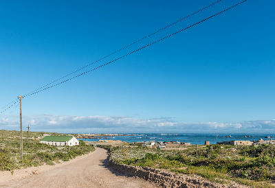 Dirt road leading into Tietiesbaai at Cape Columbine Nature Reserve, with coastal vegetation, Atlantic Ocean views and granite shoreline visible near Paternoster, South Africa.