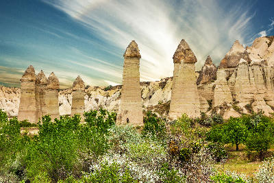 Towering fairy chimneys at Paşabağ (Monks Valley) in Cappadocia, Turkey, rising above green vegetation beneath dramatic streaked clouds in Göreme National Park.