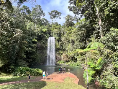 Visitors beside the plunge pool below Millaa Millaa Falls amid tropical rainforest in Queensland, Australia.