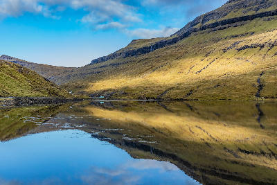 Still water reflections on Leynavatn lake surrounded by terraced hills on Streymoy, Faroe Islands.