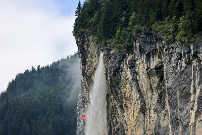 Staubbach Falls flowing down a tall rock face with mist and forest in Lauterbrunnen Valley Switzerland
