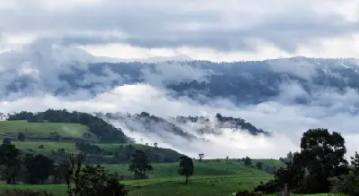 Mist and low clouds drifting between forested mountains above rolling green farmland in the Atherton Tablelands, Queensland.