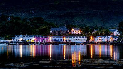 Night view of Portree Harbour on the Isle of Skye, with harbour lights reflecting on calm water.