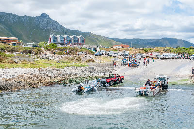 Fishing boats being pulled from the water at Kleinmond Harbour with mountains and coastal buildings in the background in South Africa.