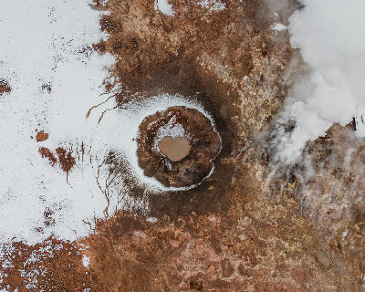 Top-down view of a steaming mud pool at Gunnuhver geothermal area on the Reykjanes Peninsula, Iceland, with mineral-stained ground and patches of snow.
