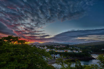 Aerial view over Portree on the Isle of Skye before sunset, with the harbour and surrounding landscape in soft evening light.