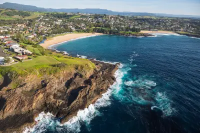 Aerial view across Kiama’s rocky headland, sheltered beaches and blue Pacific Ocean, with the coastal town and Illawarra escarpment beyond.
