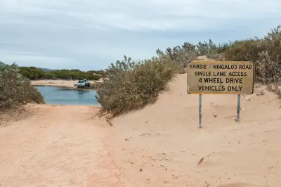 Four-wheel-drive vehicle approaches a creek crossing beside a sign marking 4WD-only access at Yardie Creek.