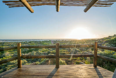 Wooden terrace overlooking coastal fynbos and ocean at sunset near Cape Agulhas, South Africa.