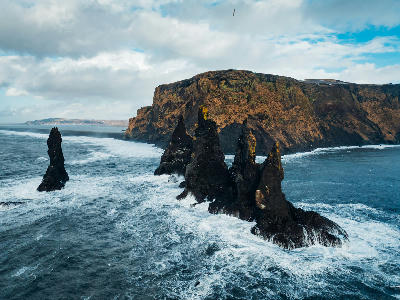 Reynisdrangar basalt sea stacks on Iceland’s South Coast, standing in rough Atlantic waters below steep coastal cliffs near Vík.