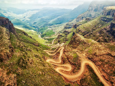 Aerial view of the winding gravel road on Sani Pass climbing through steep mountain valleys and cliffs in the Drakensberg between South Africa and Lesotho.