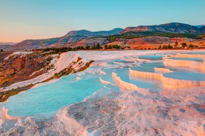 White travertine terraces filled with turquoise thermal water at Pamukkale, with rugged mountains rising in the background.