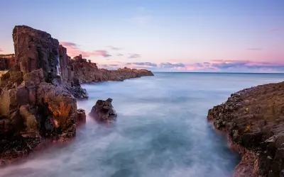 Long-exposure seascape of rugged basalt columns rising beside the ocean at Bombo Headland Quarry near Kiama, New South Wales.
