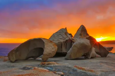 Remarkable Rocks granite formations silhouetted against a vivid orange sunset, with sunlight breaking between the weathered boulders above the Southern Ocean on Kangaroo Island.