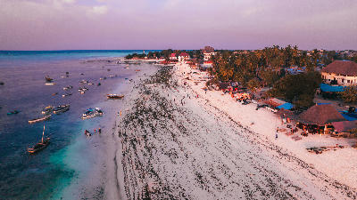Aerial view of Nungwi Beach at sunset with anchored boats, white sand, palm-lined shoreline and visitors enjoying the beach, Zanzibar, Tanzania.