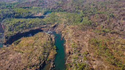 Aerial view of the Mitchell River winding through rugged sandstone gorges toward Mitchell Falls, with Big Mertens Falls visible in the distance.