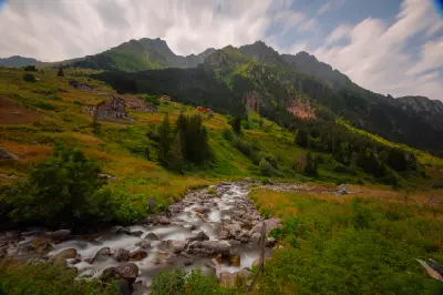 Rocky mountain stream, alpine meadows and scattered houses beneath rugged peaks at Elevit Plateau in the Kaçkar Mountains, Turkey.