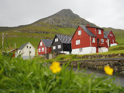 Red and black wooden houses in Mikladalur village on Kalsoy in the Faroe Islands with mountain backdrop.
