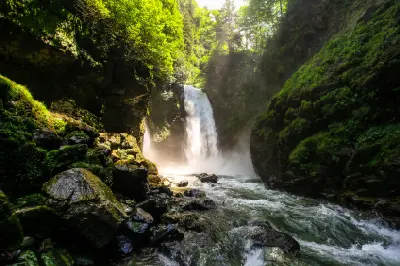 Palovit Waterfall plunging into a rocky forest gorge as sunlight filters through the trees and illuminates the spray in Rize, Turkey.