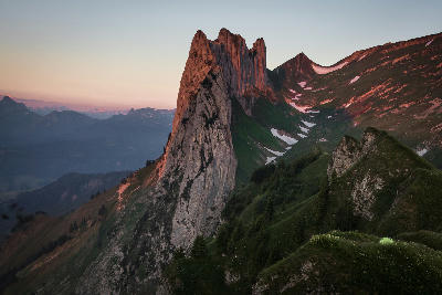 Sunset light illuminating the steep limestone rock formations of Saxer Lücke in the Alpstein mountains, Switzerland, with layered ridges and distant peaks.