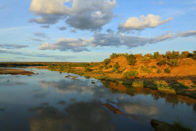 Sunset light reflecting on the Letaba River in Kruger National Park with dramatic clouds, sandy riverbanks and riverine vegetation.