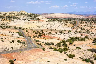 Winding paved road crossing pale sandstone hills and desert vegetation in Grand Staircase-Escalante, Utah.