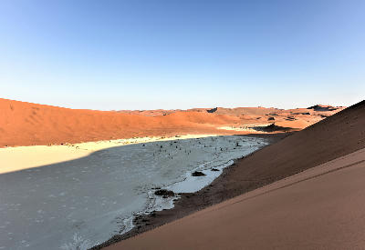 White clay pan and scattered dead trees surrounded by red sand dunes in Hiddenvlei, Namibia’s Namib Desert.