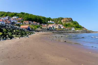 Sandy beach leading towards the hillside cottages and rocky headland of Runswick Bay in North Yorkshire, England.