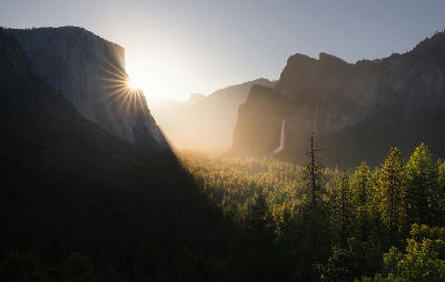Tunnel View Yosemite Valley California with El Capitan, Bridalveil Fall and sun rays illuminating forest and granite cliffs at sunrise.