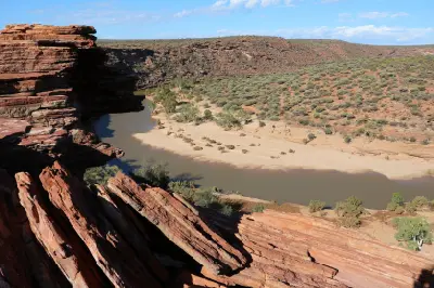 Red sandstone formations overlook the Murchison River and sandy riverbank within the rugged Z Bend gorge.