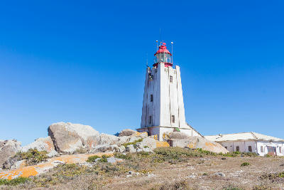 Cape Columbine Lighthouse standing among granite boulders and coastal vegetation near Paternoster on South Africa’s West Coast under a clear blue sky.