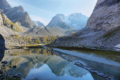 Stepping stones crossing Lac des Vaches with alpine peaks and glacier in the background in Vanoise National Park