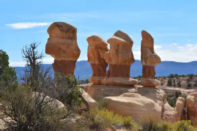 Group of tall sculpted sandstone hoodoos rising above desert vegetation at Devil’s Garden beneath a clear blue sky.