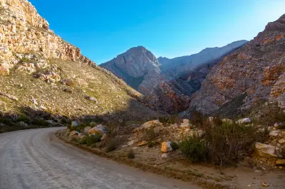 Gravel road passing through steep sandstone cliffs and rugged mountain scenery in Seweweekspoort, Klein Karoo, South Africa.