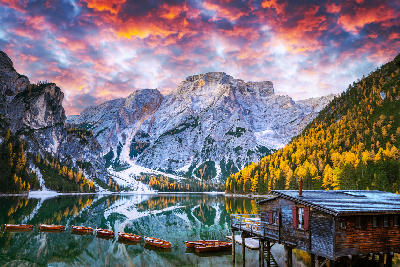 Autumn sunset at Lago di Braies, with wooden boats and a pier reflected in clear water beneath the Dolomite mountains, Italy.