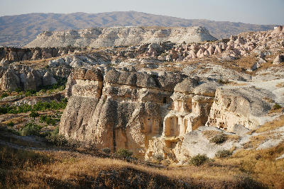 Rock-cut cave dwellings overlooking Rose Valley in Cappadocia, Turkey, with pink volcanic ridges, fairy chimneys and layered cliffs in the background.
