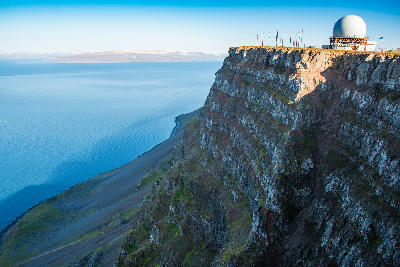 Steep coastal cliffs at Bolafjall in the Westfjords of Iceland, with a radar dome on the cliff edge and the fjord stretching into the distance below.