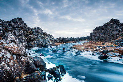 Öxará River flowing between basalt rift cliffs in Thingvellir National Park, Golden Circle, Iceland, during winter with snow and ice along the banks.