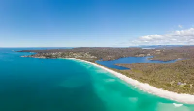 Aerial view of Binalong Bay showing turquoise ocean, white-sand beach, coastal settlement and inland lagoons in Tasmania.