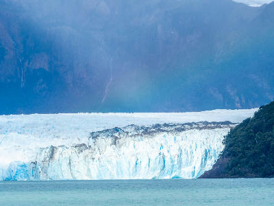Wide view of Spegazzini Glacier ice wall meeting a glacial lake with dark mountain backdrop in Patagonia, Argentina.