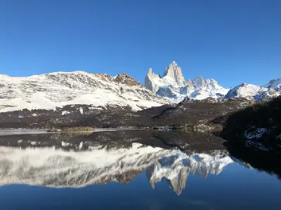 Mount Fitz Roy reflected in still water at Laguna Capri with snow-covered landscape in Patagonia, Argentina.