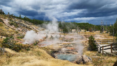 Boiling mud pots and steam rising from geothermal vents with colorful mineral deposits in Yellowstone National Park, Wyoming.