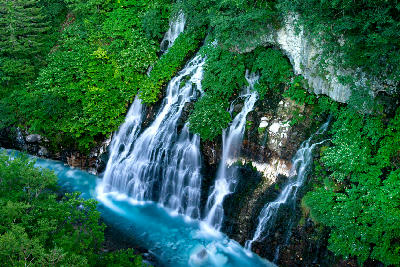Detail of Shirahige Falls streams flowing over rock into a light blue river in Biei Hokkaido Japan