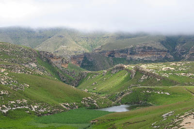 Green mountain valleys, sandstone escarpments and a small wetland lake beneath low cloud in the Golden Gate and Maluti foothills region of the eastern Free State, South Africa.