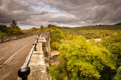 View along the stone parapet and walkway of Lambley Viaduct, with black railings, autumn-coloured trees and the River South Tyne valley below.
