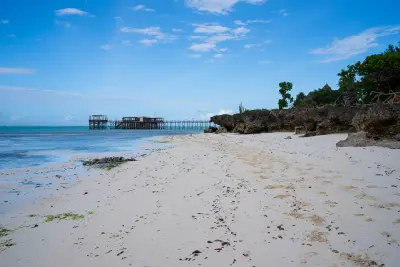 White sand beach and rocky shoreline with a wooden jetty extending into the Indian Ocean at Nungwi, Zanzibar, Tanzania.