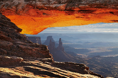 View through Mesa Arch with glowing underside framing distant canyon spires and layered desert terrain in Canyonlands National Park Utah