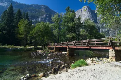 Sentinel Bridge crossing the Merced River with trees and granite cliffs in Yosemite Valley.