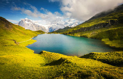 Bachalpsee alpine lake with clear blue water, surrounded by green slopes and snow-covered peaks in the Bernese Alps, Switzerland.